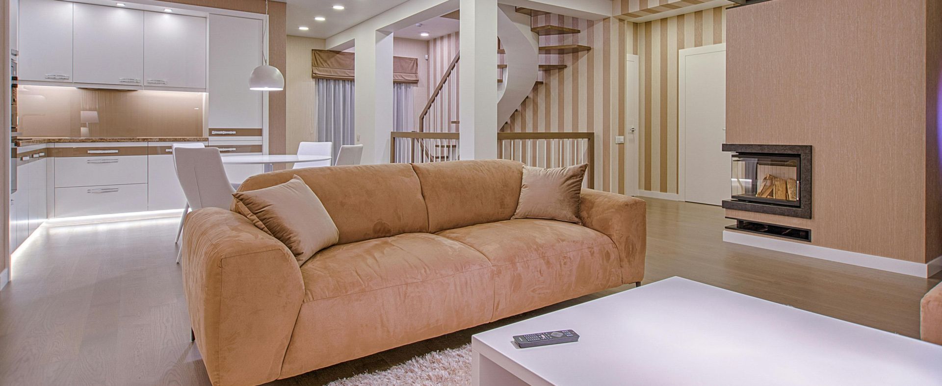 Luxurious living room with modern interior design, featuring beige sofa, fireplace, and open kitchen.