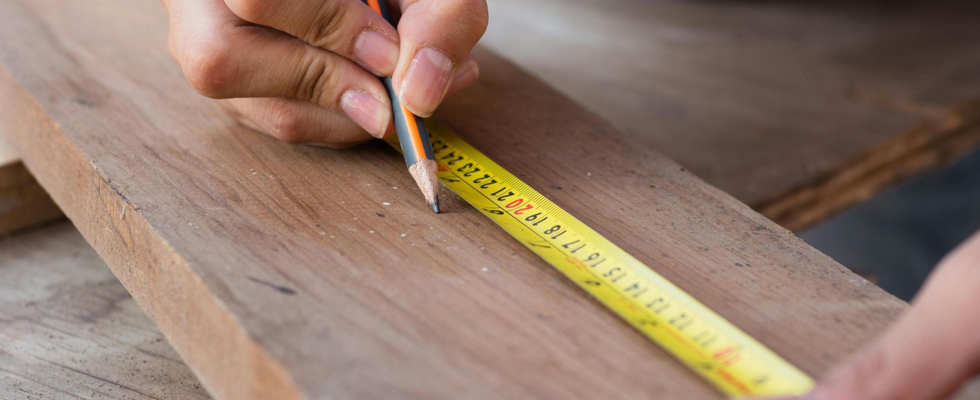 Close-up of hands using a measuring tape and pencil, highlighting precision in carpentry work.