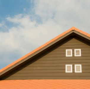 Modern house facade featuring orange roof and shuttered windows against a bright blue sky.